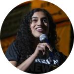 A headshot of Varshini Prakash where she is holding a microphone.